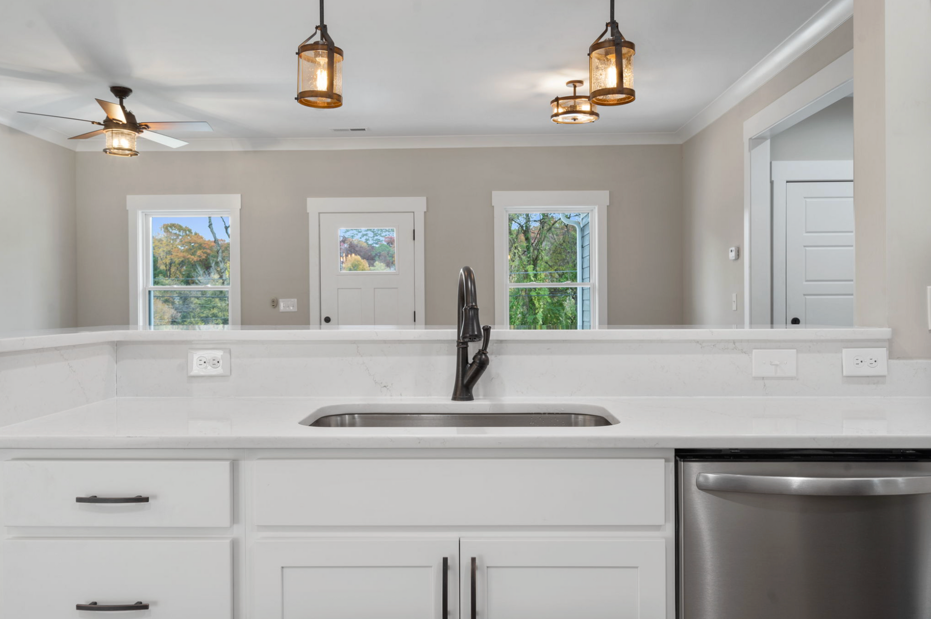 Bright modern kitchen with white cabinets, stainless sink, pendant lights, and dining area reflected ahead