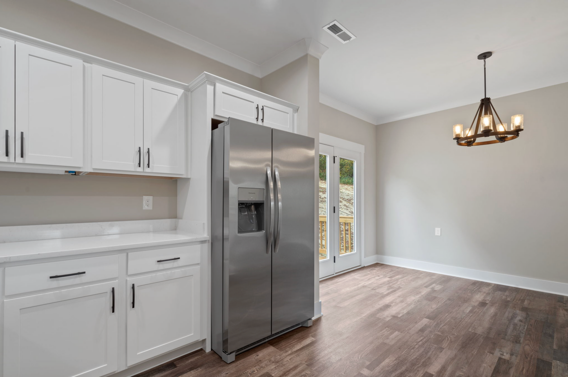 Bright kitchen with white cabinets, stainless steel fridge, hardwood floor, and dining area by glass doors