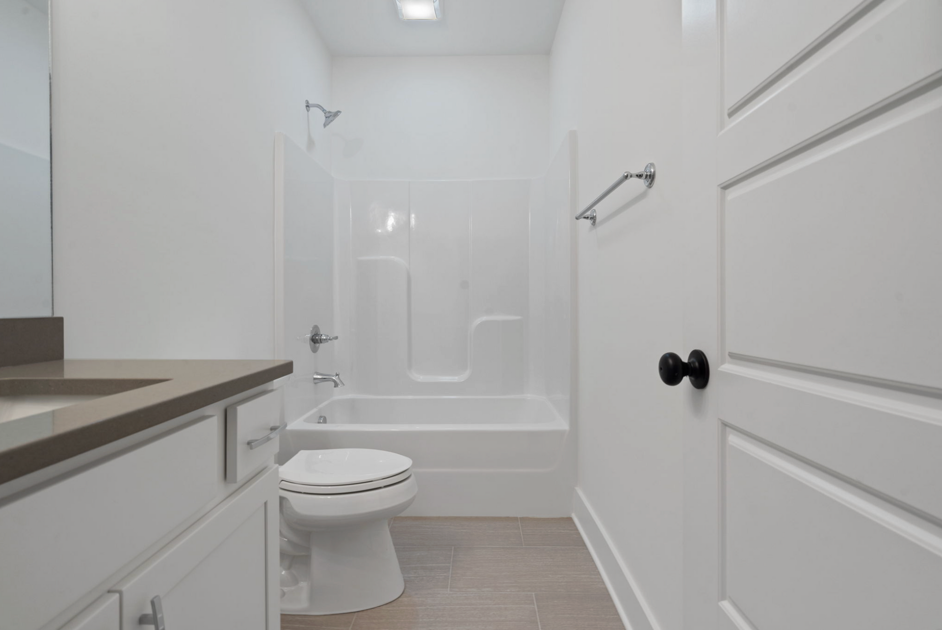 Bright white bathroom with a bathtub, toilet, vanity, and door on the right.