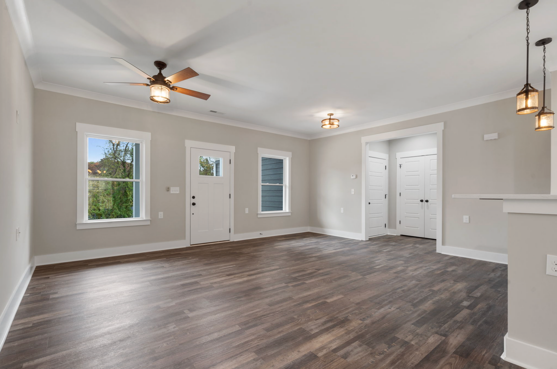 Empty living room with gray walls, dark wood floors, ceiling fans, and white trim and doors