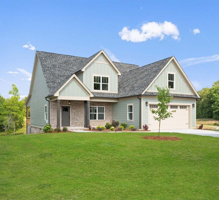 Light gray suburban house with a gabled roof, front porch, and a green lawn under a blue sky