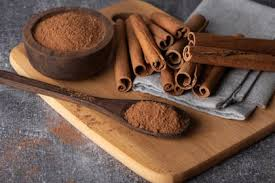 Palitos de canela y canela molida en un recipiente de madera y una cuchara sobre una tabla de cortar.