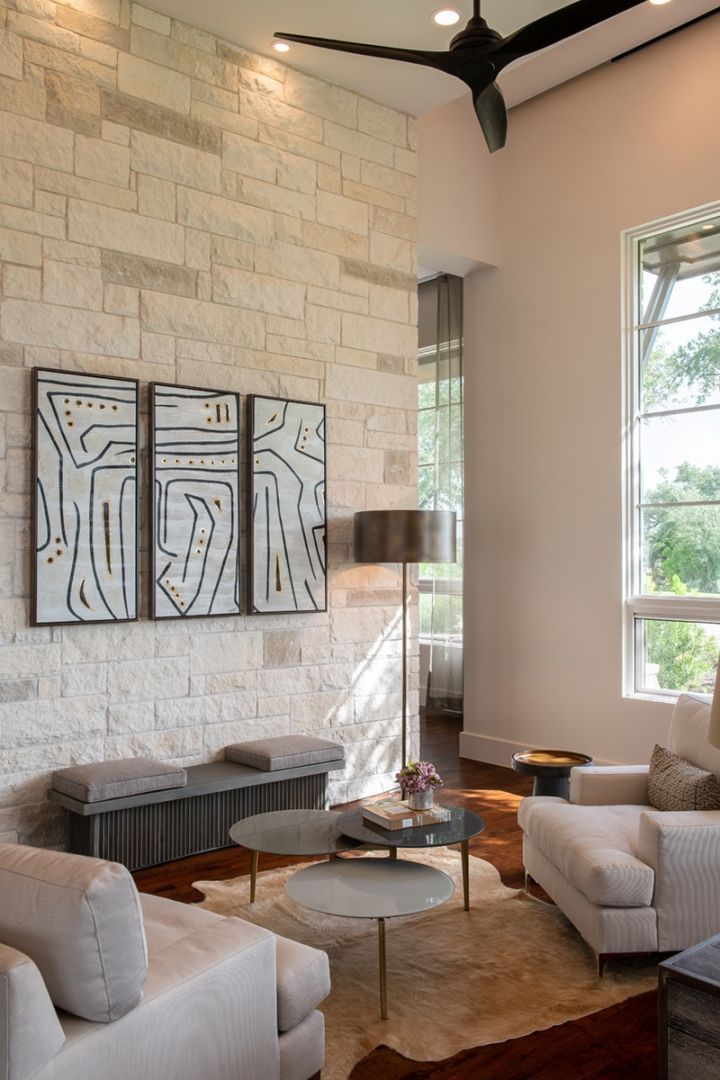 Living room with stone wall, artwork, white sofas, coffee table, and ceiling fan.