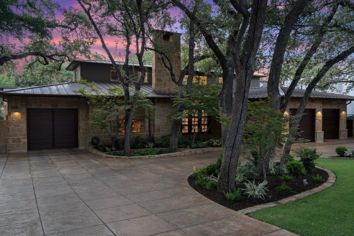 Stone-clad house with attached garages and lush landscaping under a dusk sky.