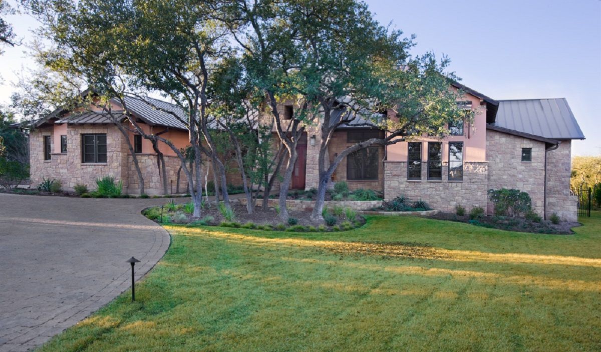 Stone and stucco house with green lawn and trees; driveway curves to the left.