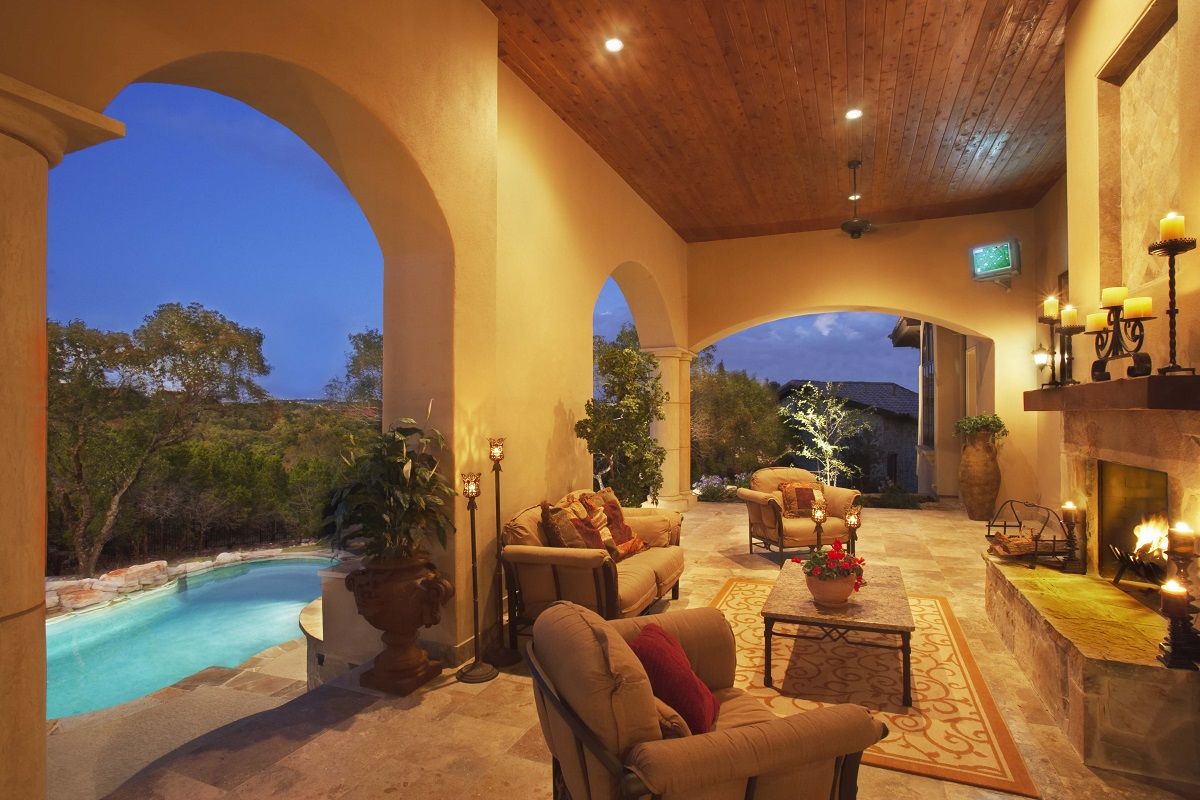 Outdoor living space with pool, arches, fireplace, seating, and lit by evening lights.