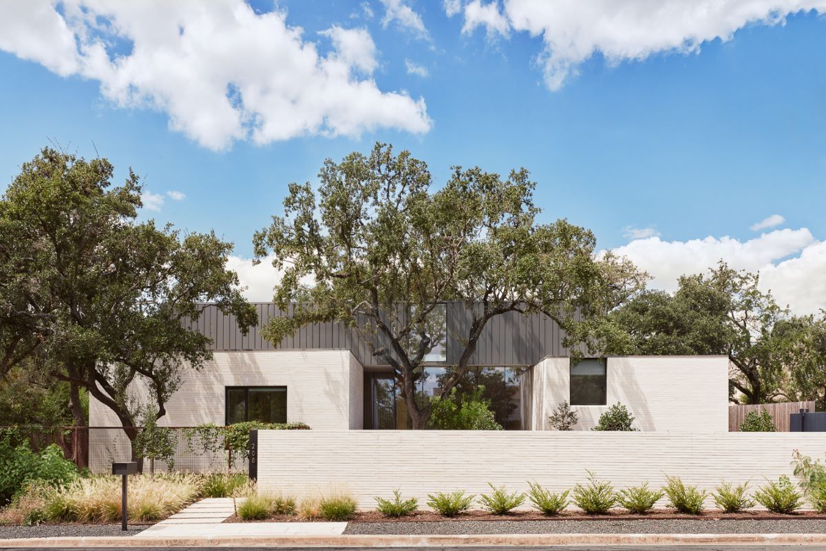 Modern home with light stone facade, large tree in front, sunny day.