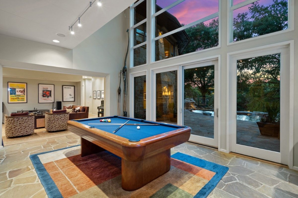 Pool table in a sunlit room with floor-to-ceiling windows overlooking a patio and sunset.