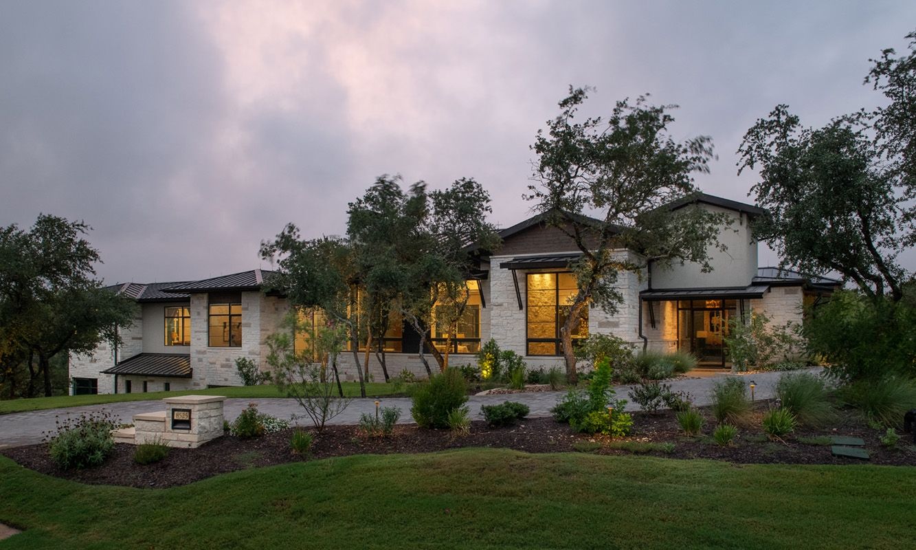 A large, light-colored house with multiple windows and a landscaped yard. Evening sky.