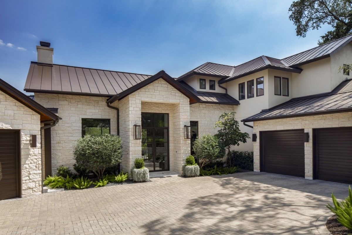 Luxurious white stone house with brown roof and driveway under a blue sky.