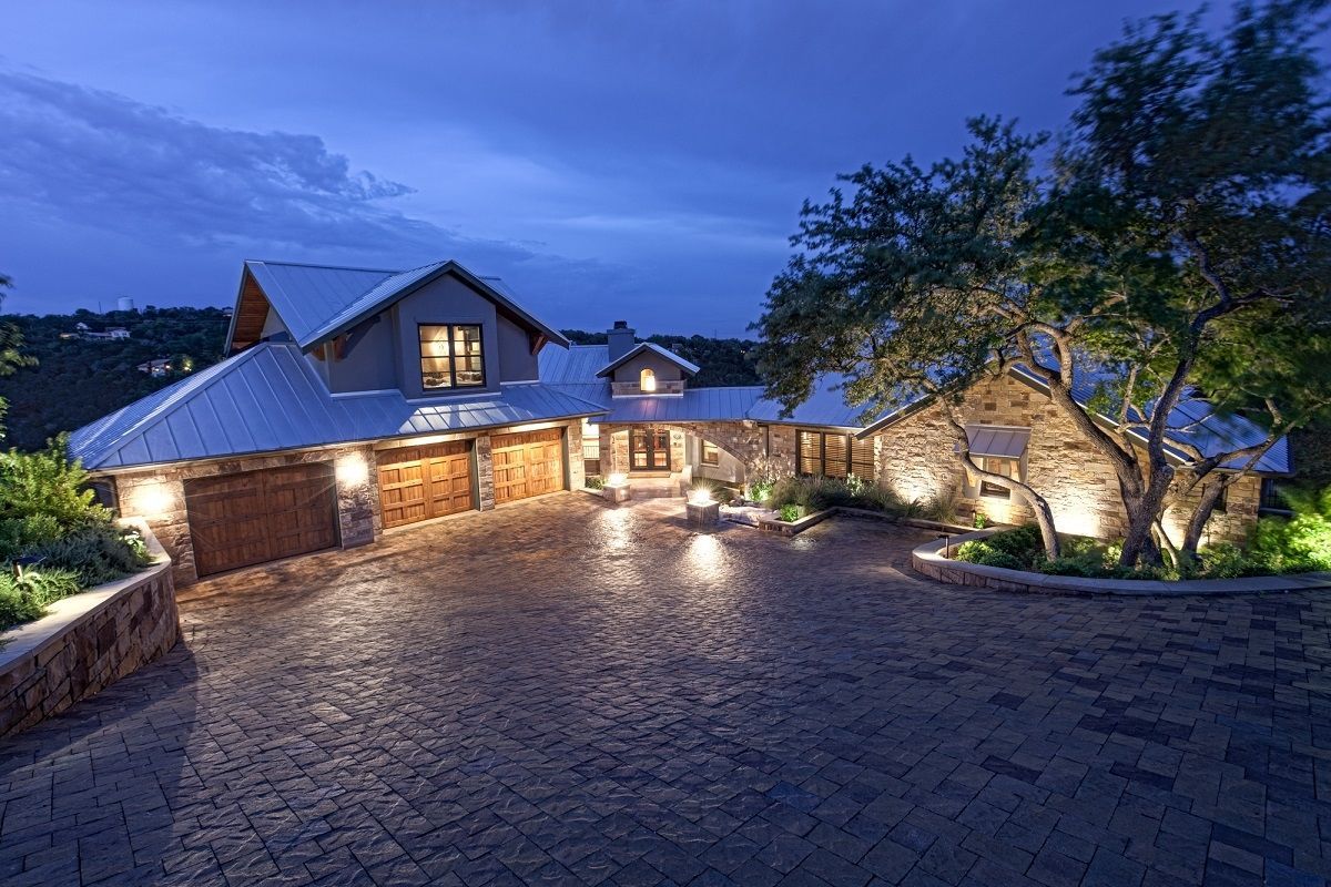 A multi-level home with a stone facade and cobblestone driveway lit up at dusk.