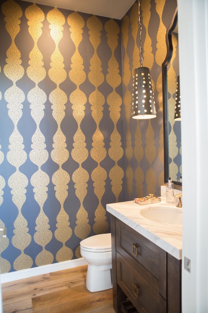Powder room with ornate gold and blue wallpaper, a wooden vanity, and a hanging light.