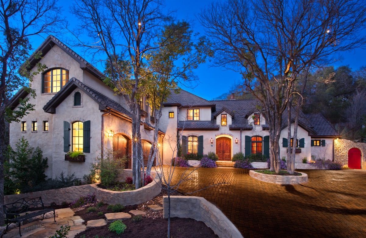 House with stucco walls, lit windows, and a dark driveway at dusk.