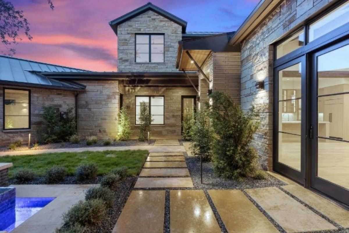 Stone house exterior with lit pathway, blue pool, and colorful sunset.