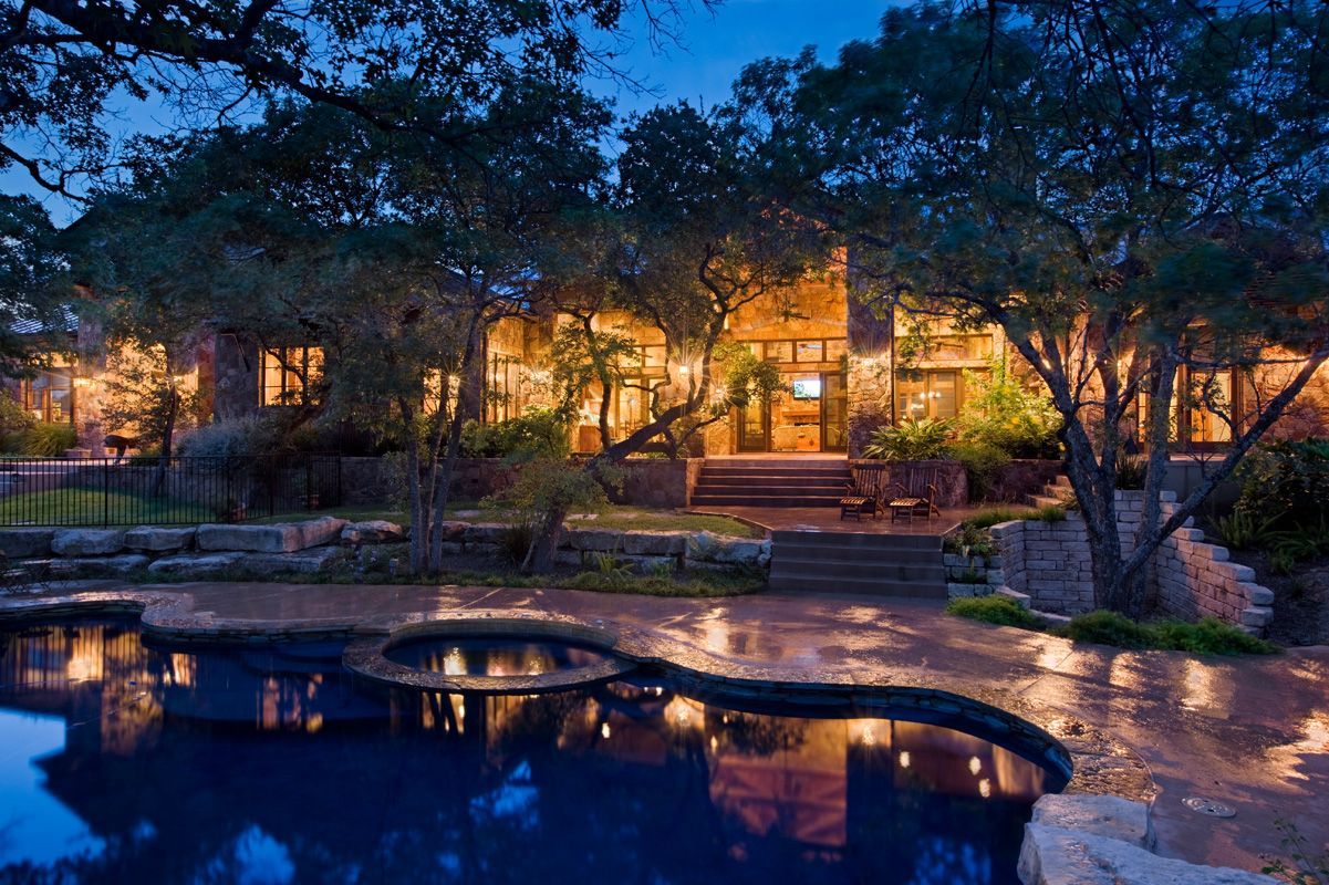 Night view of a luxurious home with a pool, trees, and soft lighting.