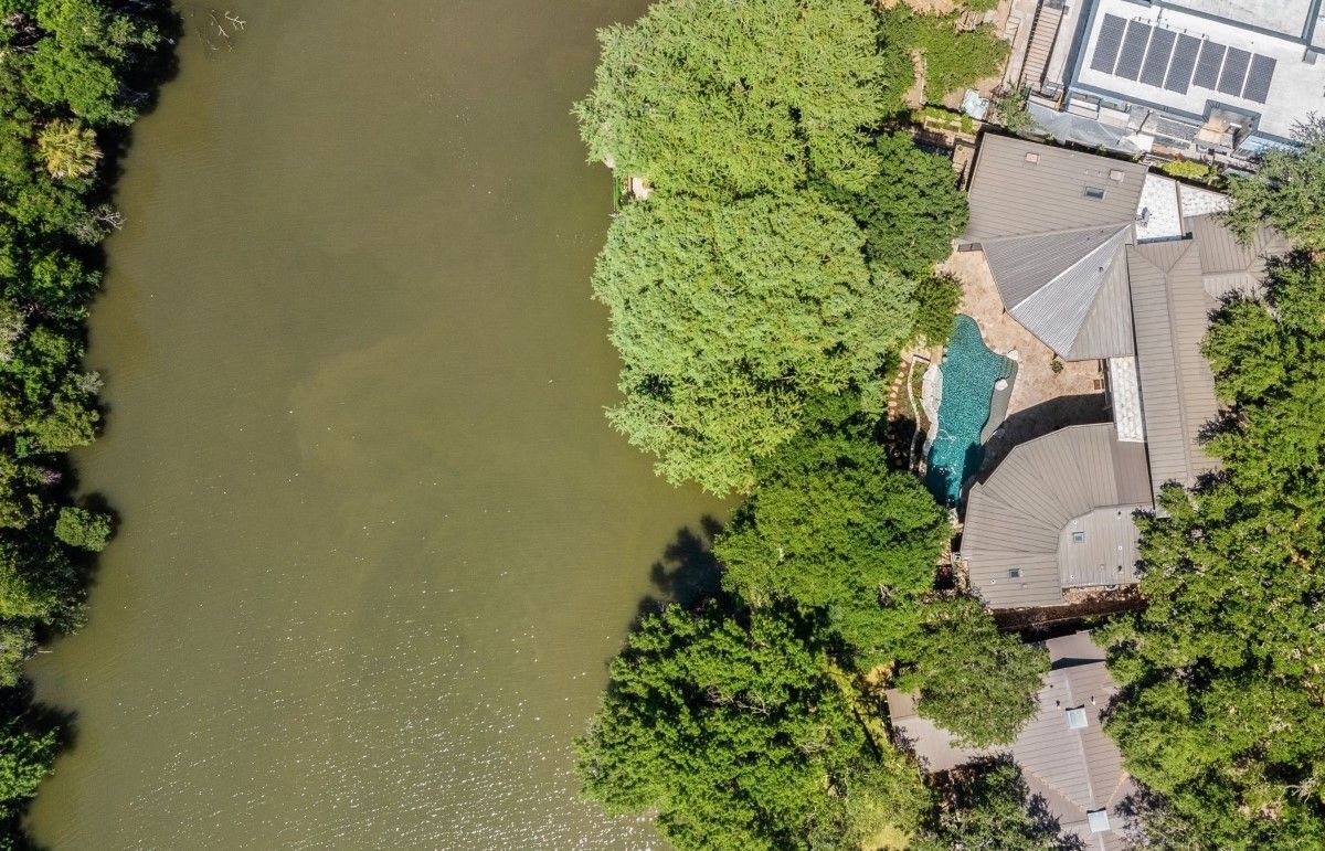Aerial view of a river next to a house shaded by trees. Solar panels are on the roof.