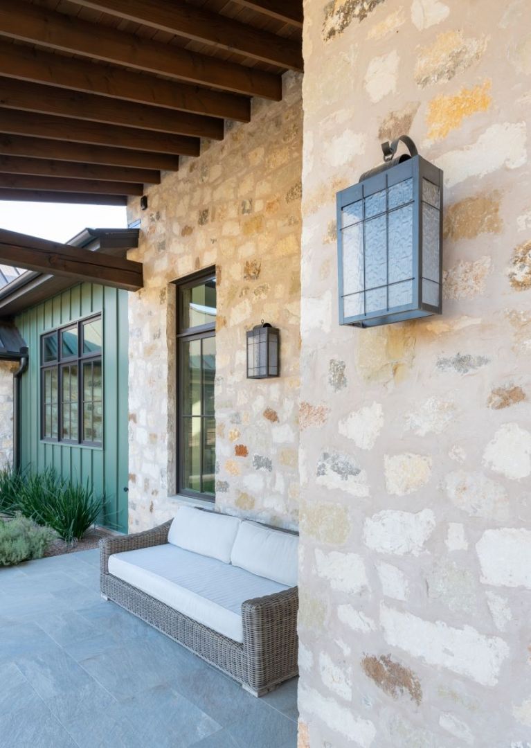 Stone exterior with porch and outdoor furniture, two wall sconces.