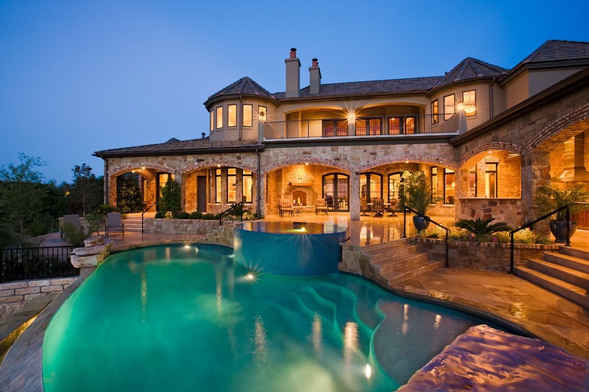 Luxury mansion with turquoise pool at dusk.