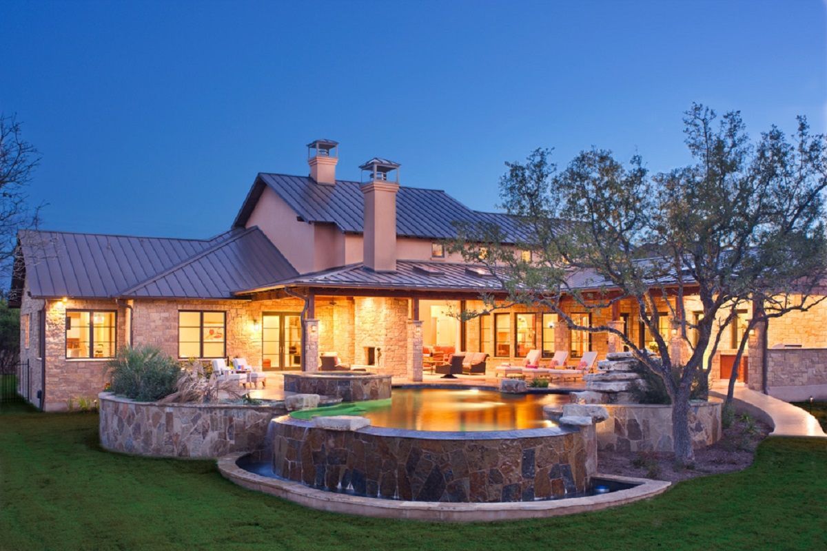 Luxury home with illuminated pool and landscaping at dusk.