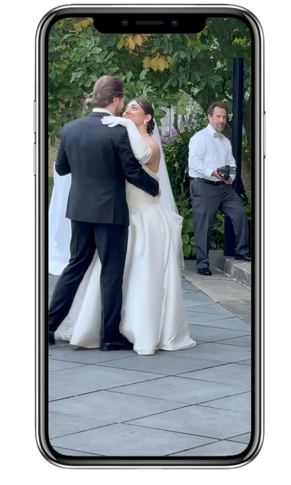 A wedding couple dances outdoors on a stone patio while a content creator captures the moment nearby.