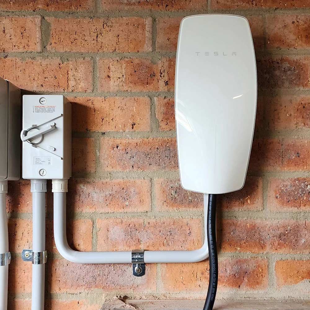 A Tesla Charging Station is Attached to a Brick Wall — Professional Electrical & Data Pty Ltd in Bonner, ACT