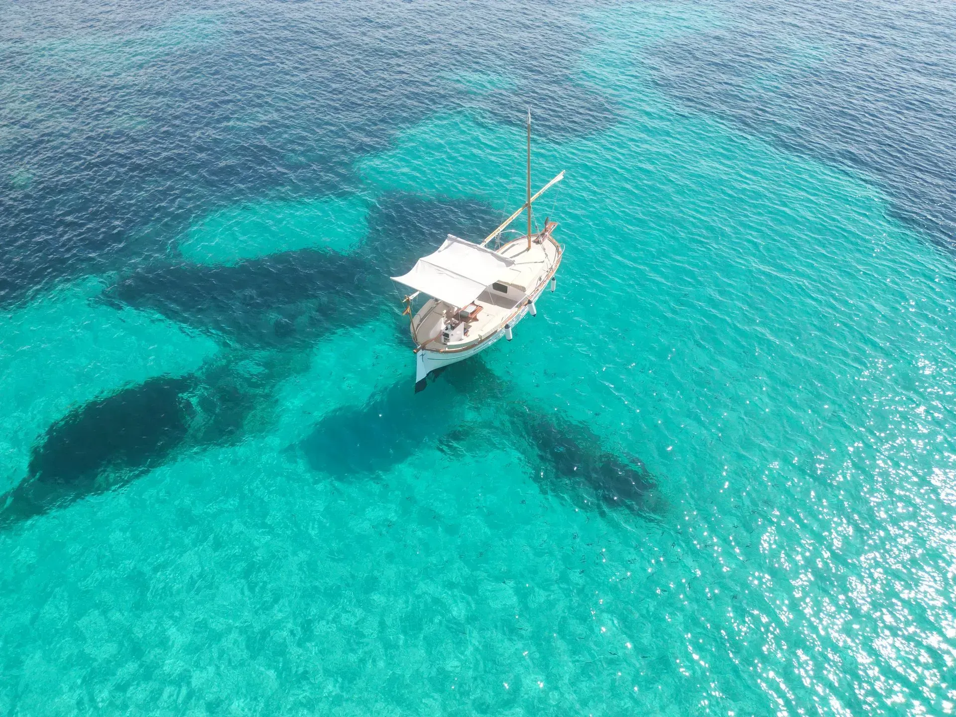 Velero anclado en aguas turquesas claras, con profundidades de un azul más oscuro más allá.
