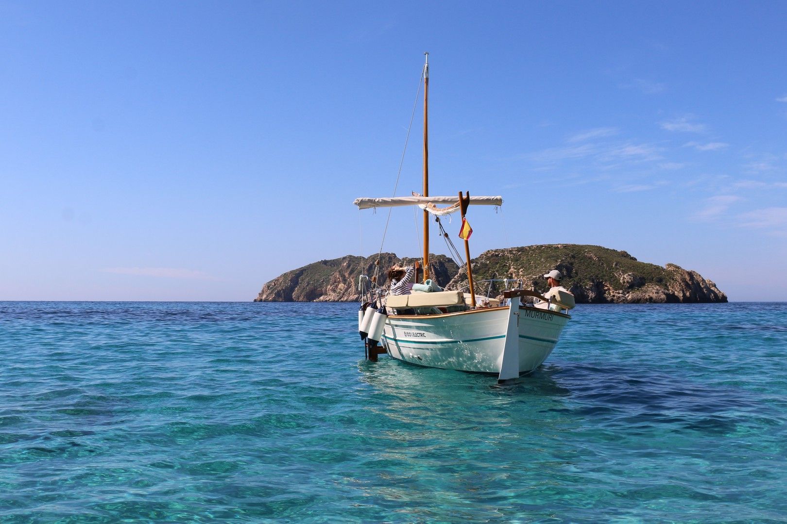 El barco flota en aguas turquesas claras, con una isla al fondo bajo un cielo azul.