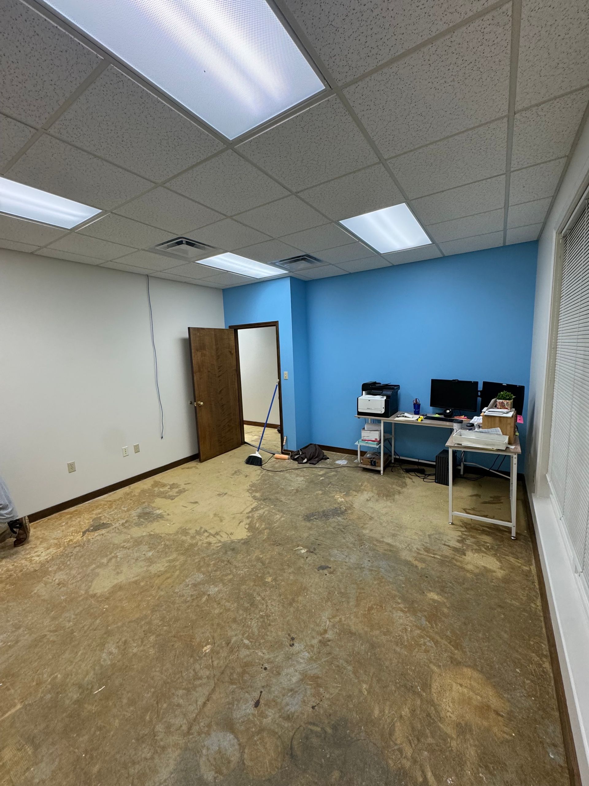 Empty office with blue and white walls, dusty floor, and a desk with computers.