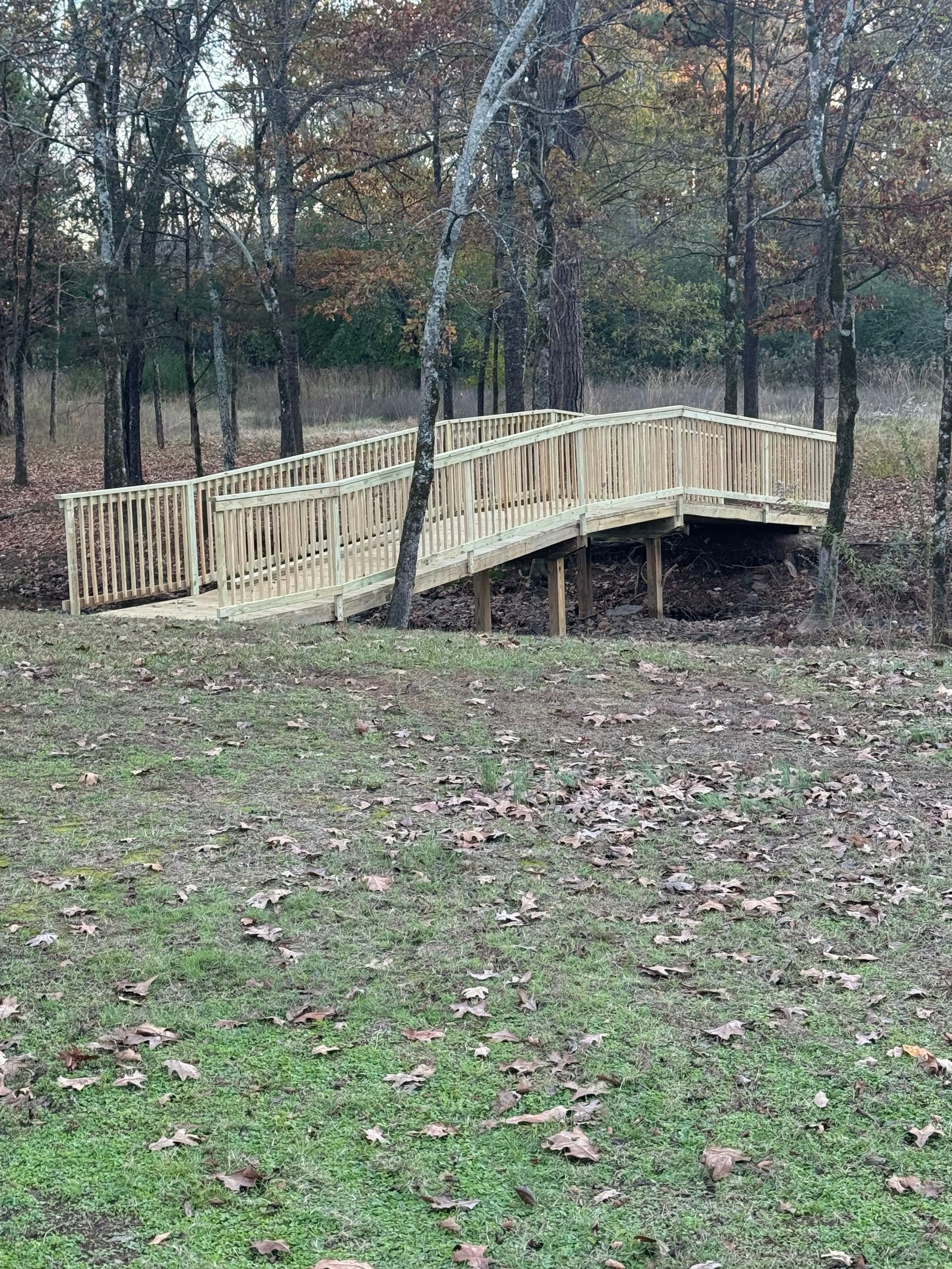 Wooden bridge over a small creek in a wooded area. The bridge is supported by wooden posts.
