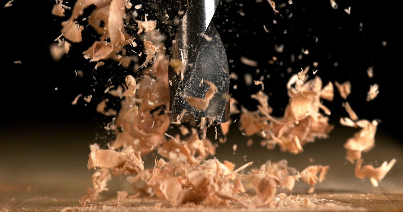 Drill bit boring into wood, creating a cloud of wood shavings against a black background.