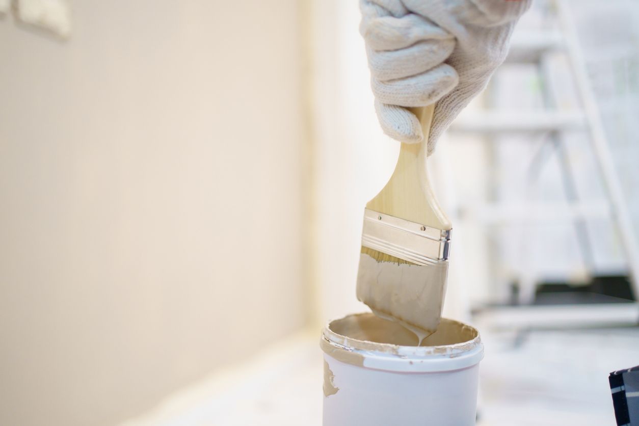 Hand in glove dipping a paint brush into a paint can; interior painting project.