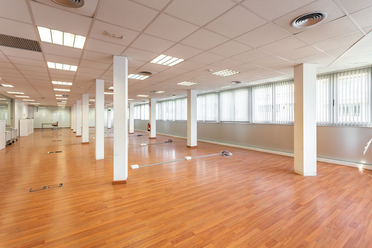 Empty office space with wood flooring, white columns, and windows with blinds.
