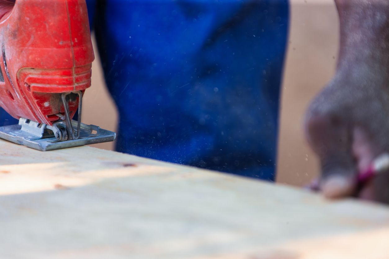 Red jigsaw cutting a piece of light wood, with blue overalls visible.