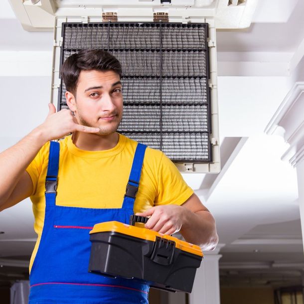 A man in overalls is holding a toolbox and making a phone call sign