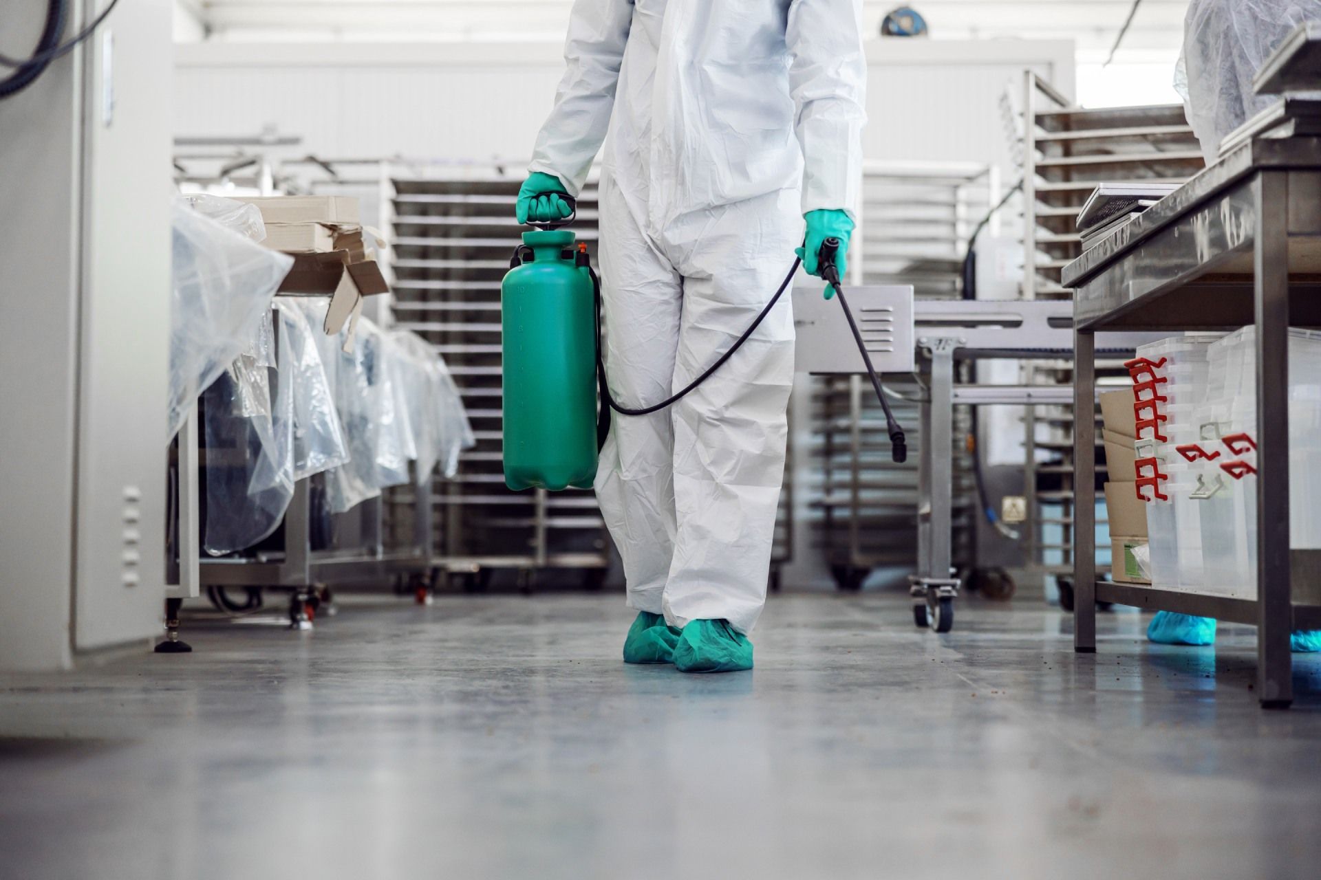 Un operaio con tuta protettiva bianca trasporta una bombola di gas verde in un laboratorio industriale sterile.