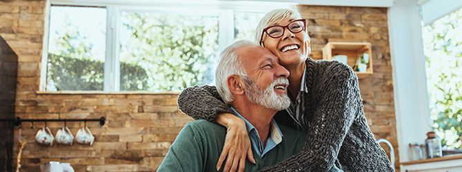 A woman is hugging an older man in a kitchen.