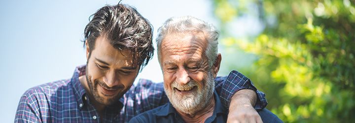 A young man is hugging an older man in a park.