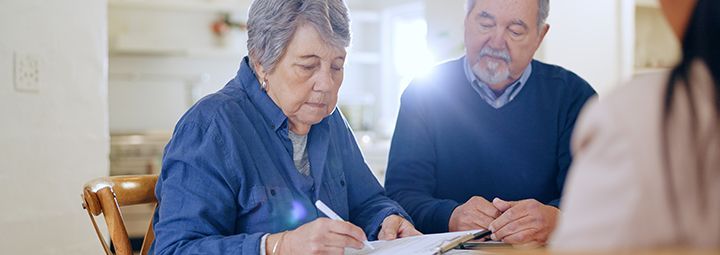 An elderly couple is sitting at a table signing a document.