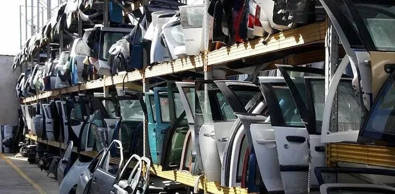 File di portiere e pannelli della carrozzeria impilati su scaffali industriali in un magazzino.