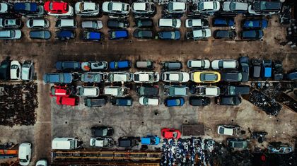 Veduta aerea di auto e furgoni parcheggiati uno accanto all'altro in un parcheggio fangoso, con file di veicoli blu, bianchi e rossi.