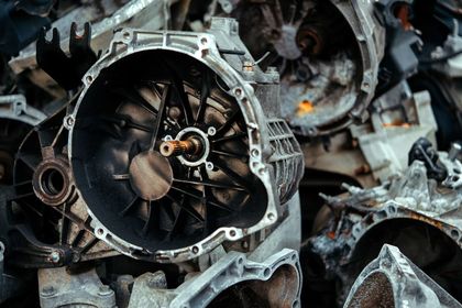 Primo piano di una pila di componenti metallici di motore e cambio, con un componente circolare a forma di ventola al centro.