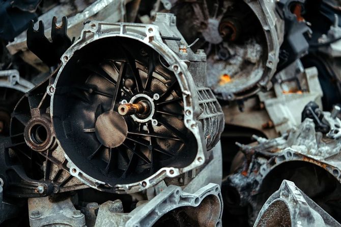 Primo piano di una pila di componenti metallici di motore e cambio, con un componente circolare a forma di ventola al centro.
