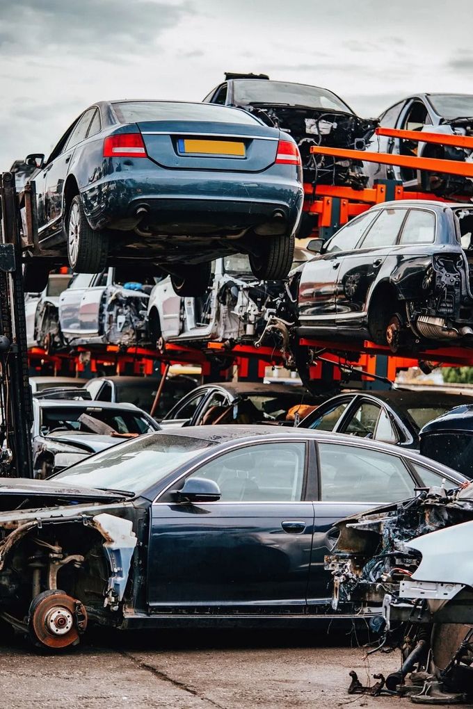 Auto incidentate accatastate in un deposito di rottami, tra cui una berlina blu e un'auto nera su scaffalature metalliche.