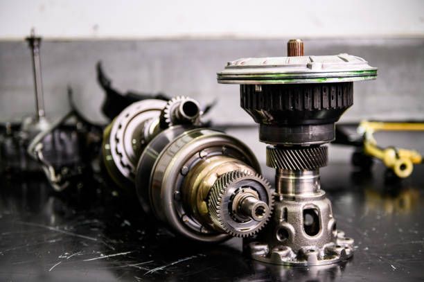 Componenti metallici di un motore automobilistico disposti su un banco da lavoro scuro, con un gruppo di ingranaggi in primo piano.