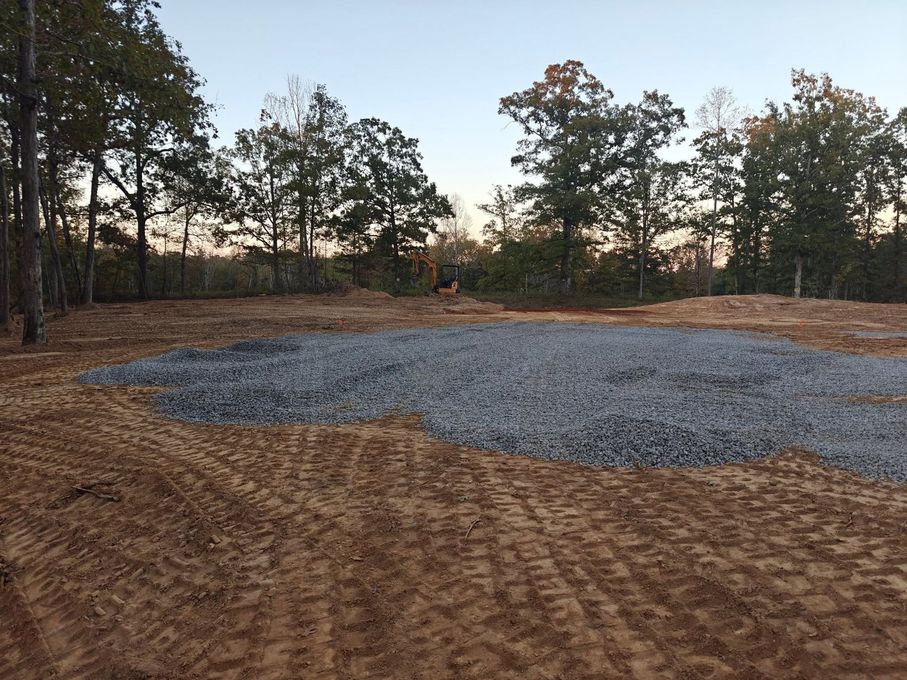 Gravel clearing in a wooded area at sunset, with trees lining the background.