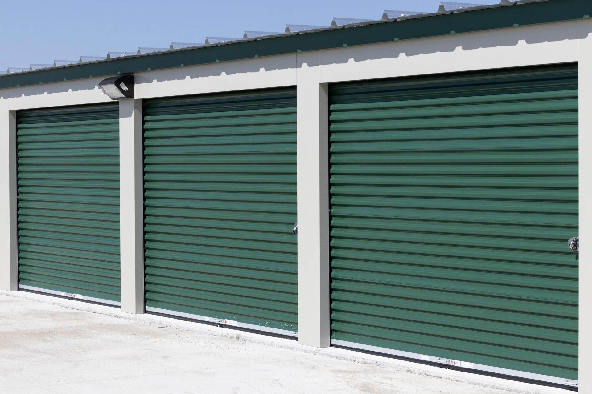 Three green roll-up storage unit doors in a row on a white building exterior