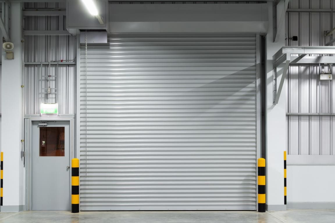 Closed gray roll-up warehouse door with black-and-yellow safety bollards in an industrial loading bay