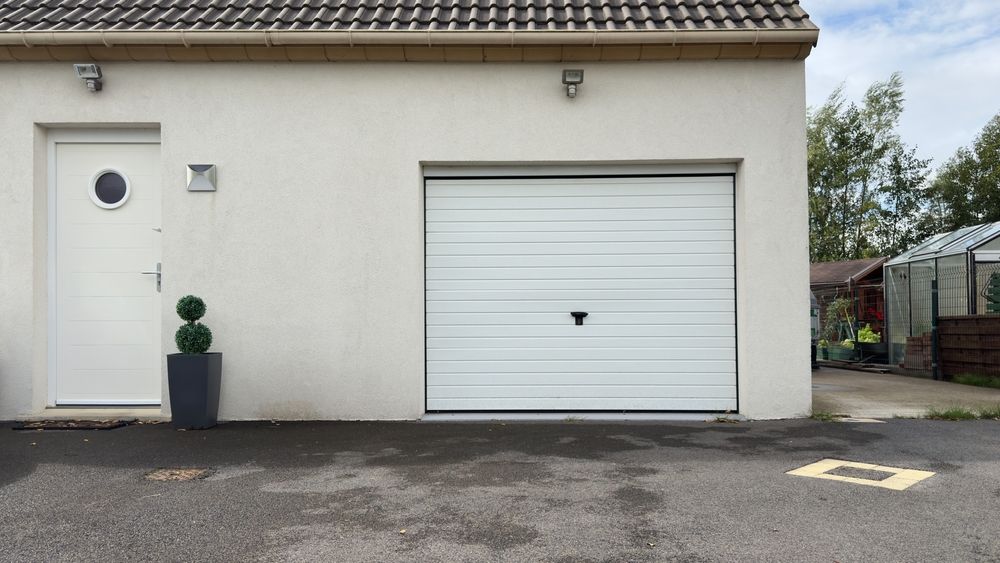 Exterior of a white house with a side door, garage door, and potted plant by the entrance