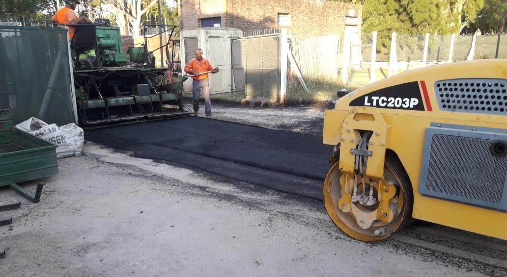 Equipo de obras viales asfaltando una calle con una apisonadora amarilla y trabajadores con chalecos naranjas