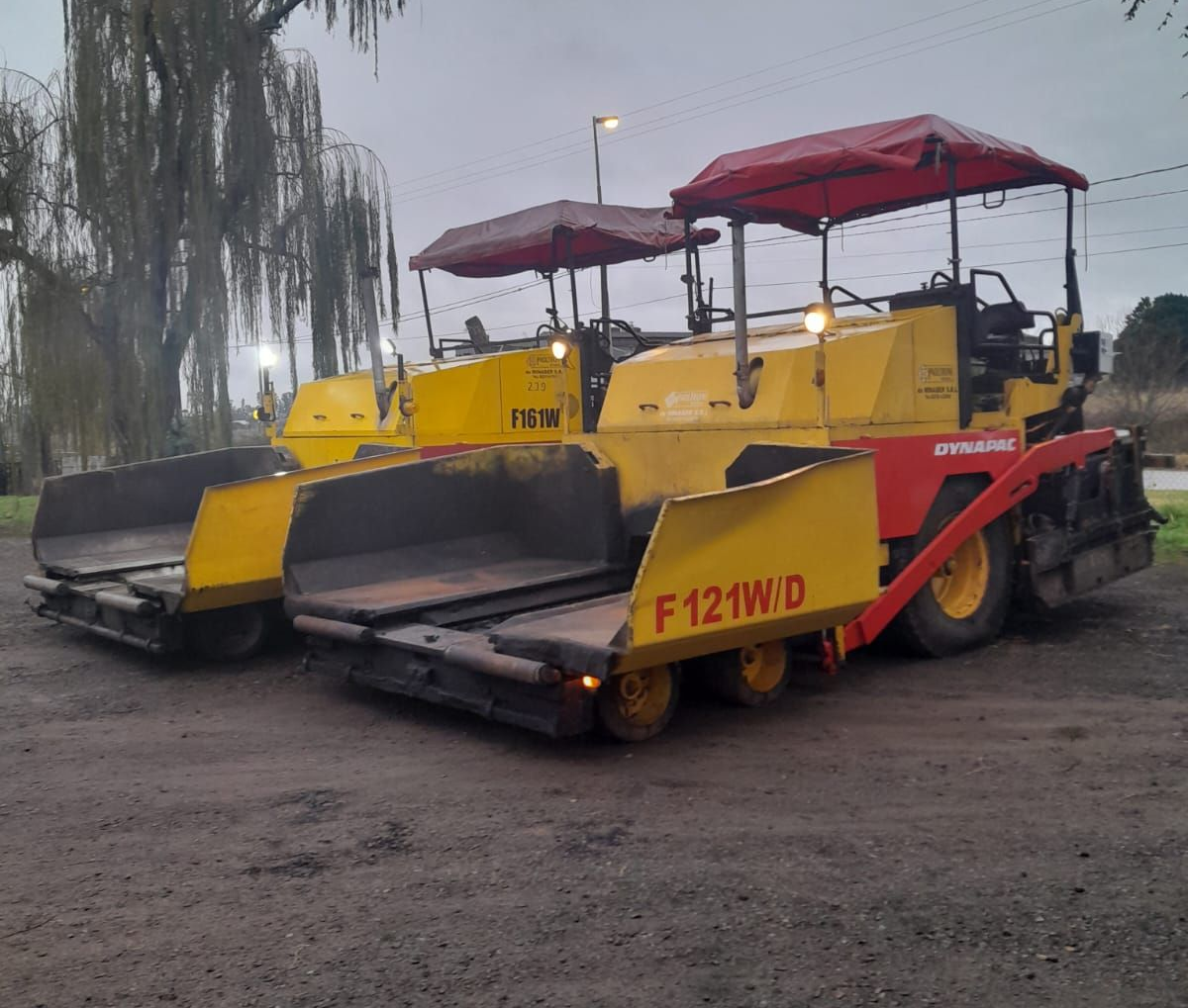 Obreros de la construcción con cascos revisan planos junto a equipos de topografía en una obra vial.